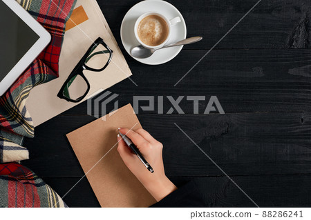 Newspaper and coffee cup, reading glasses, tablet, the hand is writing on kraft paper 88286241