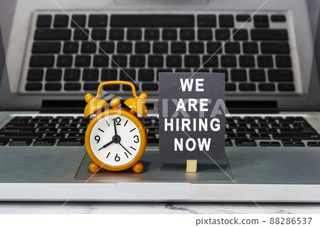 We are hiring now text on chalkboard with clock set at 8 o'clock on a laptop. 88286537