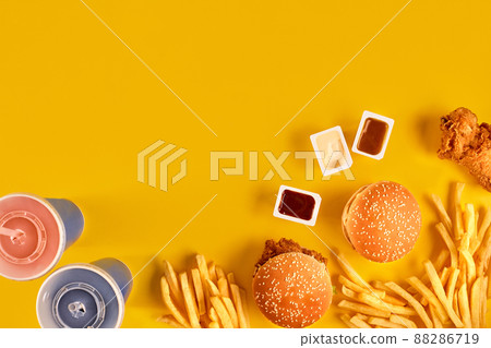 Fast food dish top view. Meat burger, potato chips and wedges. Take away composition. French fries, hamburger, mayonnaise and ketchup sauces on yellow background. 88286719