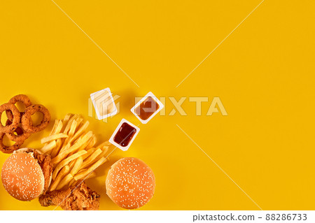 Fast food dish top view. Meat burger, potato chips and wedges. Take away composition. French fries, hamburger, mayonnaise and ketchup sauces on yellow background. Fast food dish top view. Meat burger, potato chips and wedges. Take away composition. French fries, hamburger, mayonnaise and ketchup sauces on yellow background. 88286733