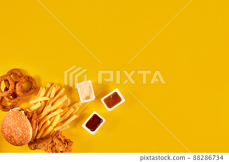 Fast food dish top view. Meat burger, potato chips and wedges. Take away composition. French fries, hamburger, mayonnaise and ketchup sauces on yellow background. Fast food dish top view. Meat burger, potato chips and wedges. Take away composition. French fries, hamburger, mayonnaise and ketchup sauces on yellow background. 88286734