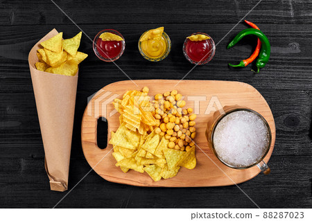 Overhead view of beer glass and snacks with sauce on black wooden table. 88287023