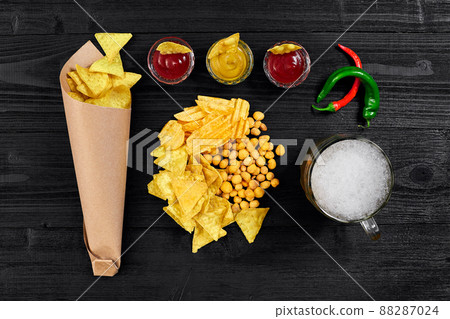 Overhead view of beer glass and snacks with sauce on black wooden table. 88287024