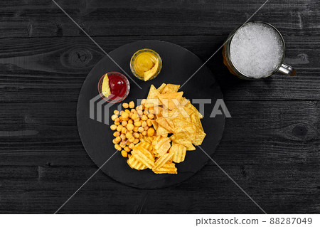 Overhead view of beer glass and snacks with sauce on black wooden table. Overhead view of beer glass and snacks with sauce on black wooden table. 88287049