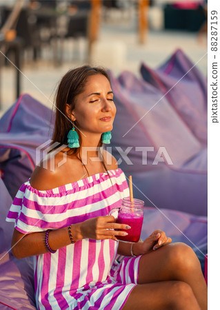 Tanned beautiful girl resting on the beach sofas and drinking a cocktail. Girl smiles and enjoys the sun. Clode up. Spa and relax concept Tanned beautiful girl resting on the beach sofas and drinking a cocktail. Girl smiles and enjoys the sun. Clode up. Spa and relax concept 88287159