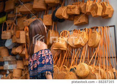 A young woman chooses a wicker bag in the store. Asian braided bags A young woman chooses a wicker bag in the store. Asian braided bags 88287165