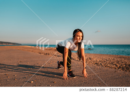 Sports and Jogging. A young brunette woman stands ready to run. In the background, the sea and the rocky shore. Copy space 88287214