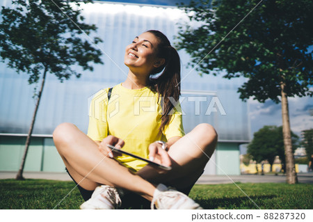 Cheerful asian female in casual wear using digital tablet recreating in city park on sunny day,  88287320