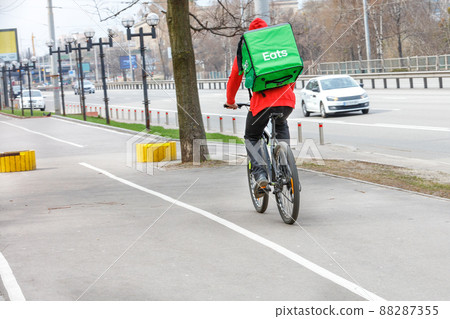 Courier with an isothermal green backpack on his back on a food delivery bike on a city street. 88287355
