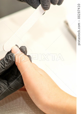 Close up of the caucasian hands of a professional manicurist are filing the nails of a young woman. Young caucasian woman receiving a manicure by a beautician with a nail file in a nail salon Close up of the caucasian hands of a professional manicurist are filing the nails of a young woman. Young caucasian woman receiving a manicure by a beautician with a nail file in a nail salon 88287410