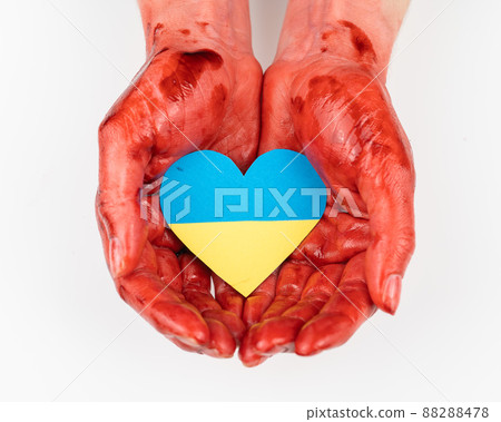 Woman with hands covered in blood holding a heart with the flag of ukraine on a white background.  88288478