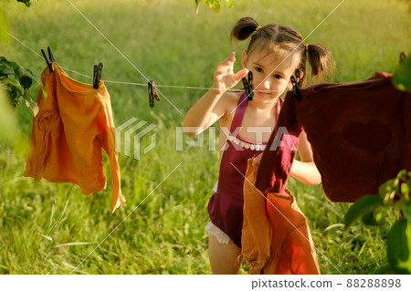 The girl reaches out with her hand to the clothespin to hang wet clothes to dry after washing. Clothes are hanging in the garden on a clothesline. Baby launder his clothes 88288898
