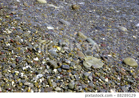 sea pebble beach with multicoloured stones, transparent waves with foam, on a warm summer day 88289129