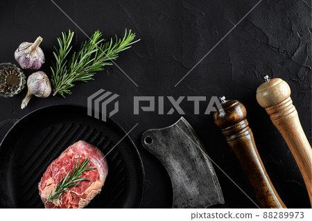 Fresh raw meat. A piece of beef tenderloin on grill pan, with a cutting ax, with spices for cooking on black stone table. Copy space Fresh raw meat. A piece of beef tenderloin on grill pan, with a cutting ax, with spices for cooking on black stone table. Copy space 88289973