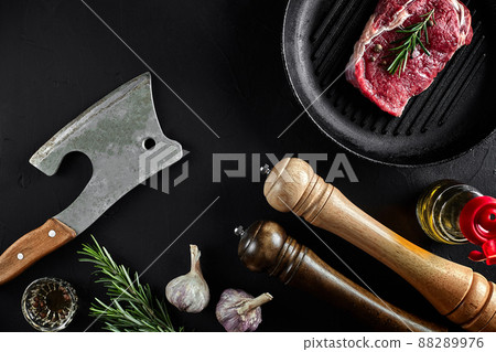 Fresh raw meat. A piece of beef tenderloin on grill pan, with a cutting ax, with spices for cooking on black stone table. Copy space Fresh raw meat. A piece of beef tenderloin on grill pan, with a cutting ax, with spices for cooking on black stone table. Copy space 88289976