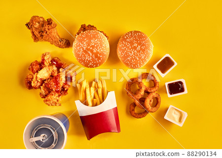 Fast food dish top view. French fries, hamburger, mayonnaise and ketchup sauces on yellow background. Fast food dish top view. French fries, hamburger, mayonnaise and ketchup sauces on yellow background. 88290134