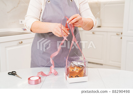 a female cook packs a Kraffin, easter cake in a box with satin ribbon a female cook packs a Kraffin, easter cake in a box with satin ribbon 88290498