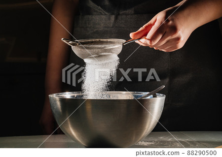 powdered sugar or flour is sifted into a bowl on a black background. powdered sugar or flour is sifted into a bowl on a black background. 88290500