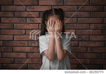 Sad little girl closing eyes with hands near brick wall. Child in danger Sad little girl closing eyes with hands near brick wall. Child in danger 88290774