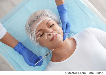 Mature woman with double chin receiving injection in clinic, above view Mature woman with double chin receiving injection in clinic, above view 88290854