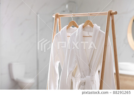 Fresh white bathrobes hanging on rack indoors Fresh white bathrobes hanging on rack indoors 88291265