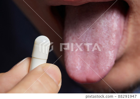 Man taking pill, mouth open with tongue sticking out. 88291947