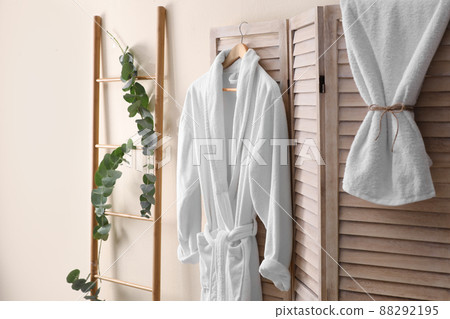 Soft comfortable bathrobe hanging on folding screen in stylish room interior Soft comfortable bathrobe hanging on folding screen in stylish room interior 88292195