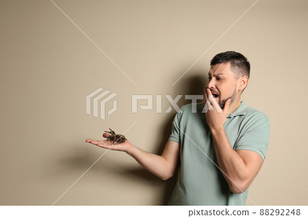 Scared man holding tarantula on beige background, space for text. Arachnophobia (fear of spiders) 88292248