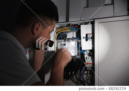 Electrician with flashlight fixing electric panel indoors 88292259