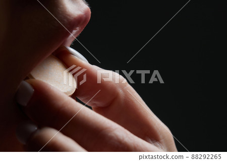 Close up of face of young woman taking drug. The drug addict is standing and putting a pill into her mouth. 88292265
