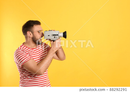 Young man using vintage video camera on yellow background, space for text Young man using vintage video camera on yellow background, space for text 88292291