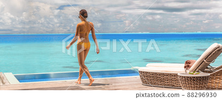 Luxury resort hotel woman walking on her private terrace deck of overwater bungalow villa with infinity pool view on turquoise ocean - honeymoon suite 88296930
