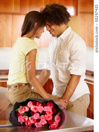 Nothing like flowers to rekindle some romance. A young couple kissing in the kitchen with roses on the counter. Nothing like flowers to rekindle some romance. A young couple kissing in the kitchen with roses on the counter. 88297485