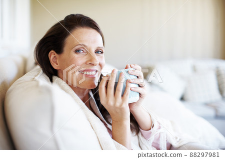 Taking a coffee break at home. Portrait of an attractive woman enjoying a cup of coffee while sitting on a sofa indoors. Taking a coffee break at home. Portrait of an attractive woman enjoying a cup of coffee while sitting on a sofa indoors. 88297981