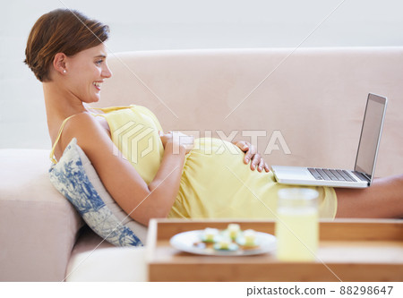 In good spirits. A smiling pregnant woman lying on the couch using a laptop with a healthy meal beside her. 88298647