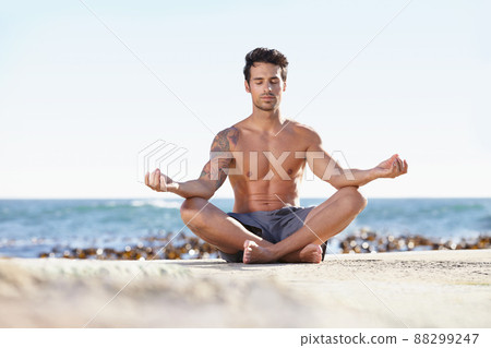 Seeking enlightenment in nature. A young man meditating next to the ocean. Seeking enlightenment in nature. A young man meditating next to the ocean. 88299247