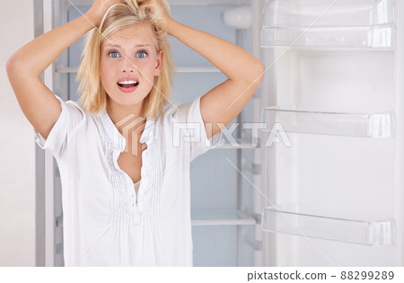 My fridge is empty. Portrait of a beautiful young woman looking in her empty fridge. My fridge is empty. Portrait of a beautiful young woman looking in her empty fridge. 88299289