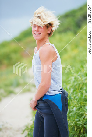 Just a classic surfer guy. Shot of a young surfer pulling on his wetsuit. 88299354