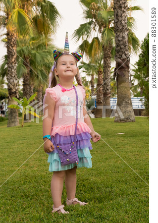 Portrait of a 4 year old girl dressed in a rainbow dress and a unicorn headband against the backdrop 88301589