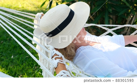 female in a straw hat is resting in a hammock around the palm trees and enjoying the tranquility and female in a straw hat is resting in a hammock around the palm trees and enjoying the tranquility and 88301593