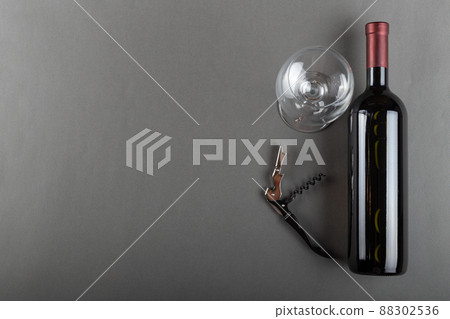 Corked red wine bottle, corkscrew and empty wine glass on gray background. Alcoholic drink. Corked red wine bottle, corkscrew and empty wine glass on gray background. Alcoholic drink. 88302536