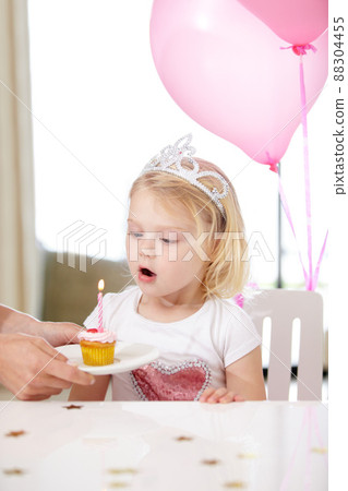 Her first birthday. Shot of a cute young girl blowing out a candle on a cupcake. Her first birthday. Shot of a cute young girl blowing out a candle on a cupcake. 88304455
