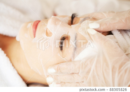 Cosmetologist applying sheet mask on woman in spa salon Cosmetologist applying sheet mask on woman in spa salon 88305826