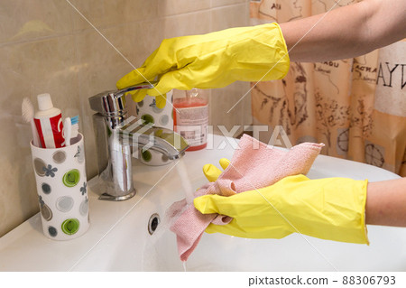 Women's hands in yellow rubber gloves wash a pink cloth under the tap 88306793