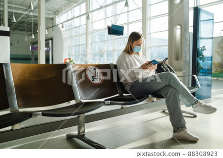 Female tourist in mask sitting in airport terminal lounge on empty marked chairs under new normal and covid social distance regulations Female tourist in mask sitting in airport terminal lounge on empty marked chairs under new normal and covid social distance regulations 88308923
