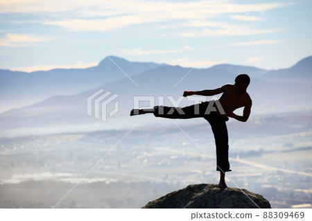 Perfect balance and technique. A male kickboxer practising his kicking technique on a mountain peak. 88309469