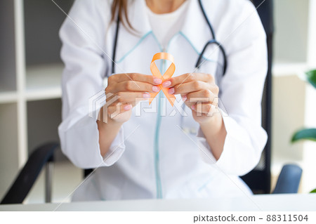Close up of a doctor holding and showing orange awareness ribbon in her hands 88311504
