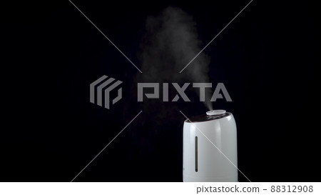 An ultrasonic humidifier humidifies a room with a strong stream of steam on an isolated black background. 88312908