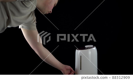 A man turned on an ultrasonic humidifier on an isolated black background. 88312909