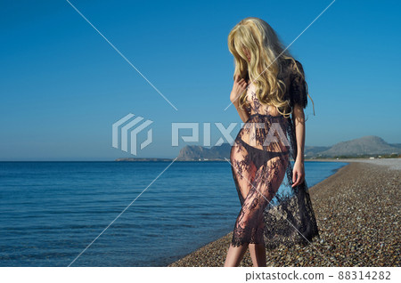 A woman in a patterned black dress on the beach. 88314282